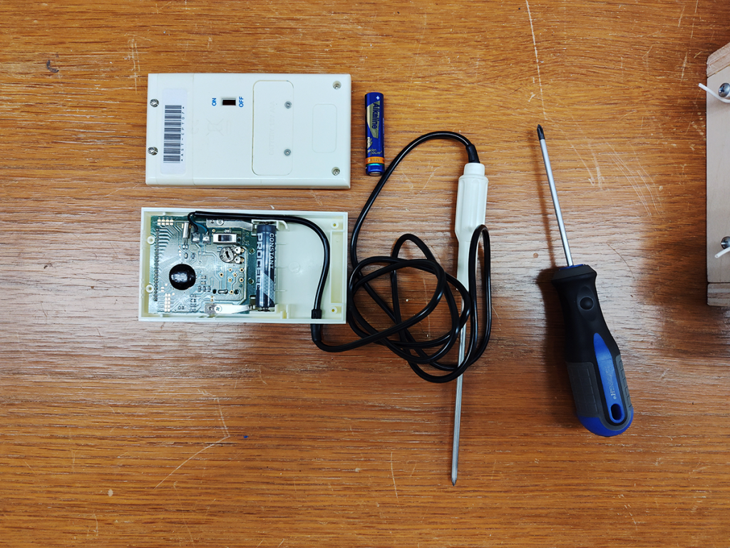 Temperature probe, open case, with circuit board, batteries, and screwdriver.