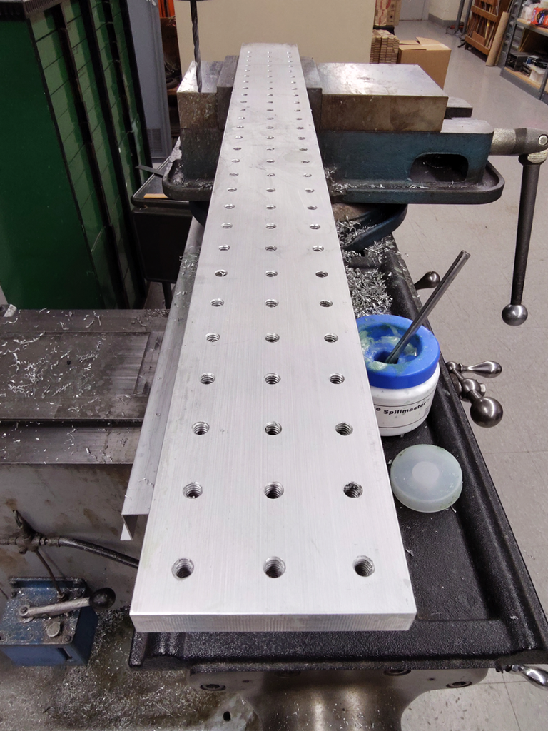 Long piece of aluminum, in process of machining mounting holes.