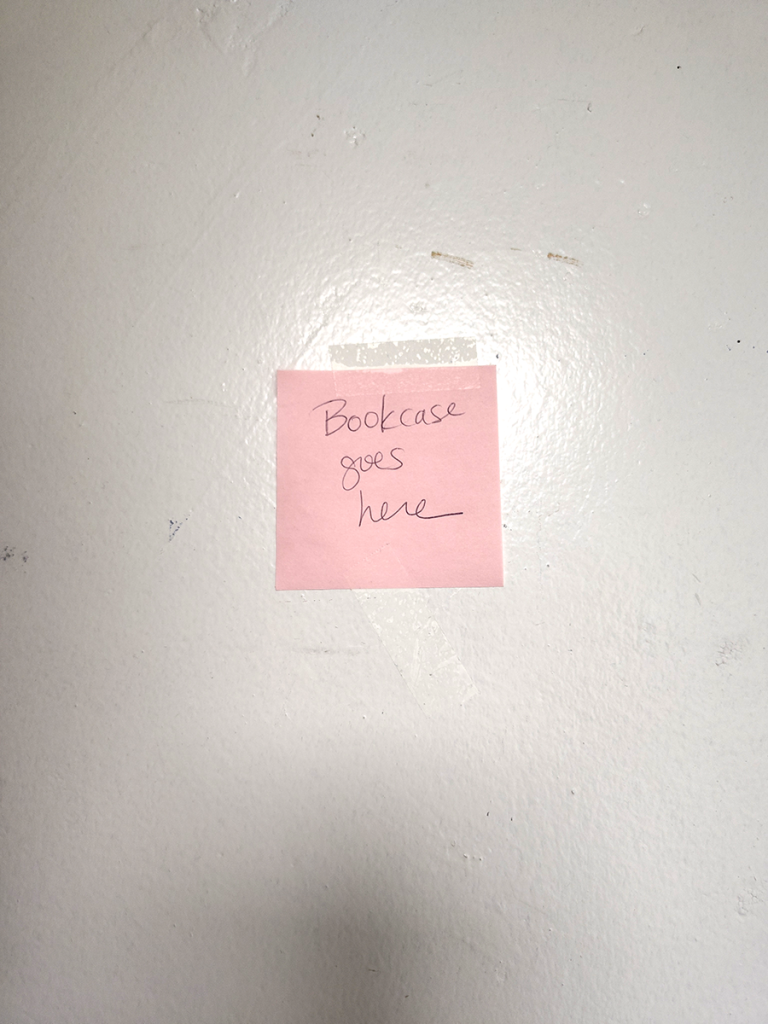 Pink handwritten note taped to the wall. "Bookcase goes here"