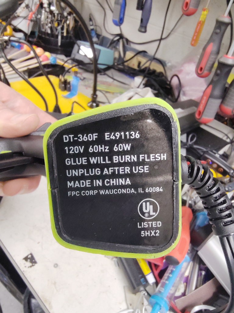 Text on underside of hot glue gun reads "Glue will burn flesh / unplug after use"