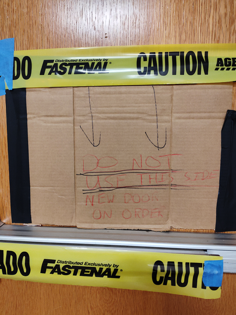 Broken door with hand-scrawled signs and caution tape.