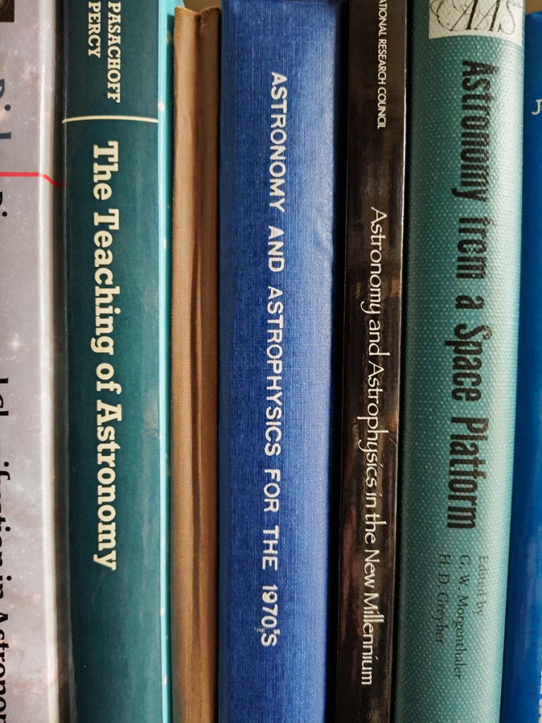 Spines of astronomy texts on a library shelf.
