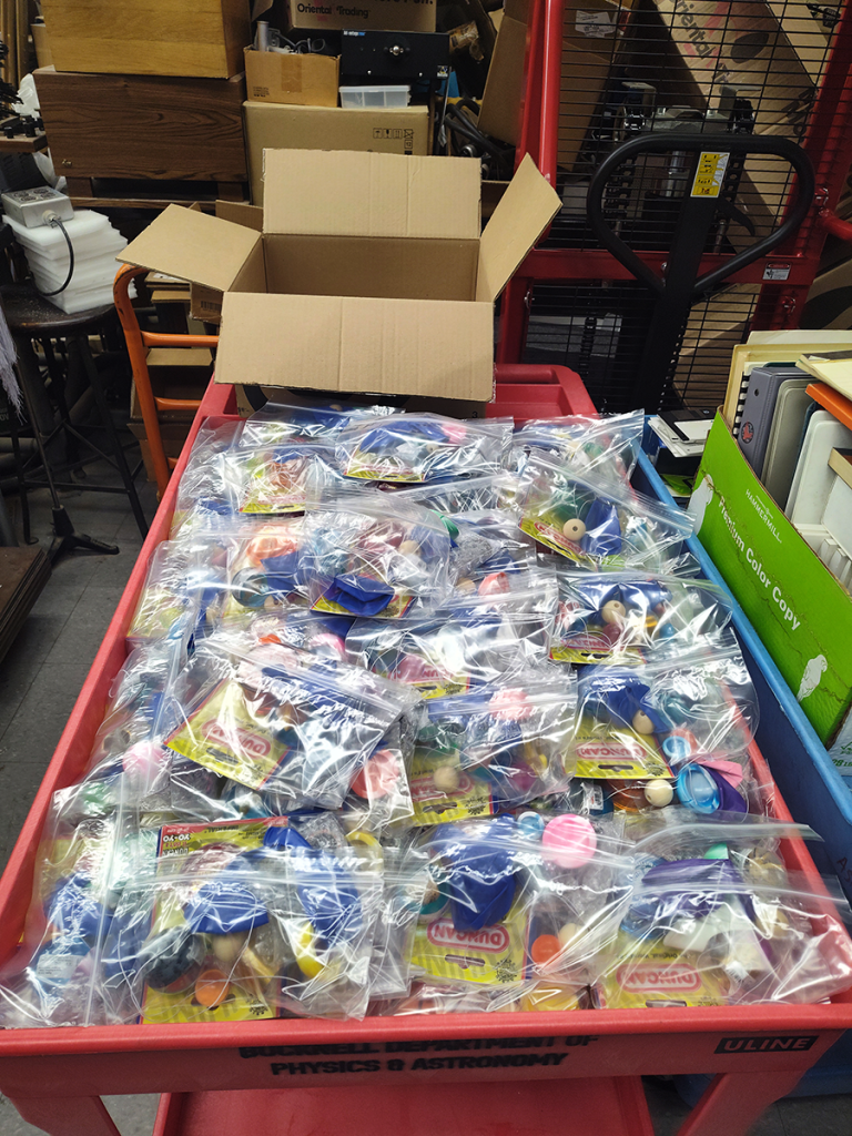 Cart loaded with plastic bags, each filled with physics toys.